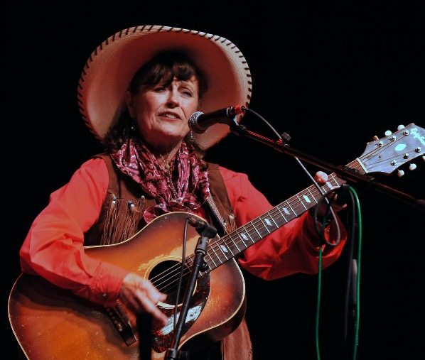 Image of Peggy Malone in a large straw hat, holding a guitar