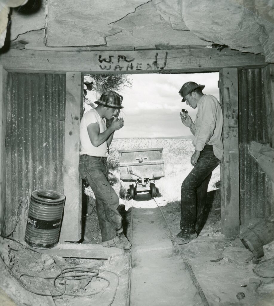 Two men smoke in a mine entrance.